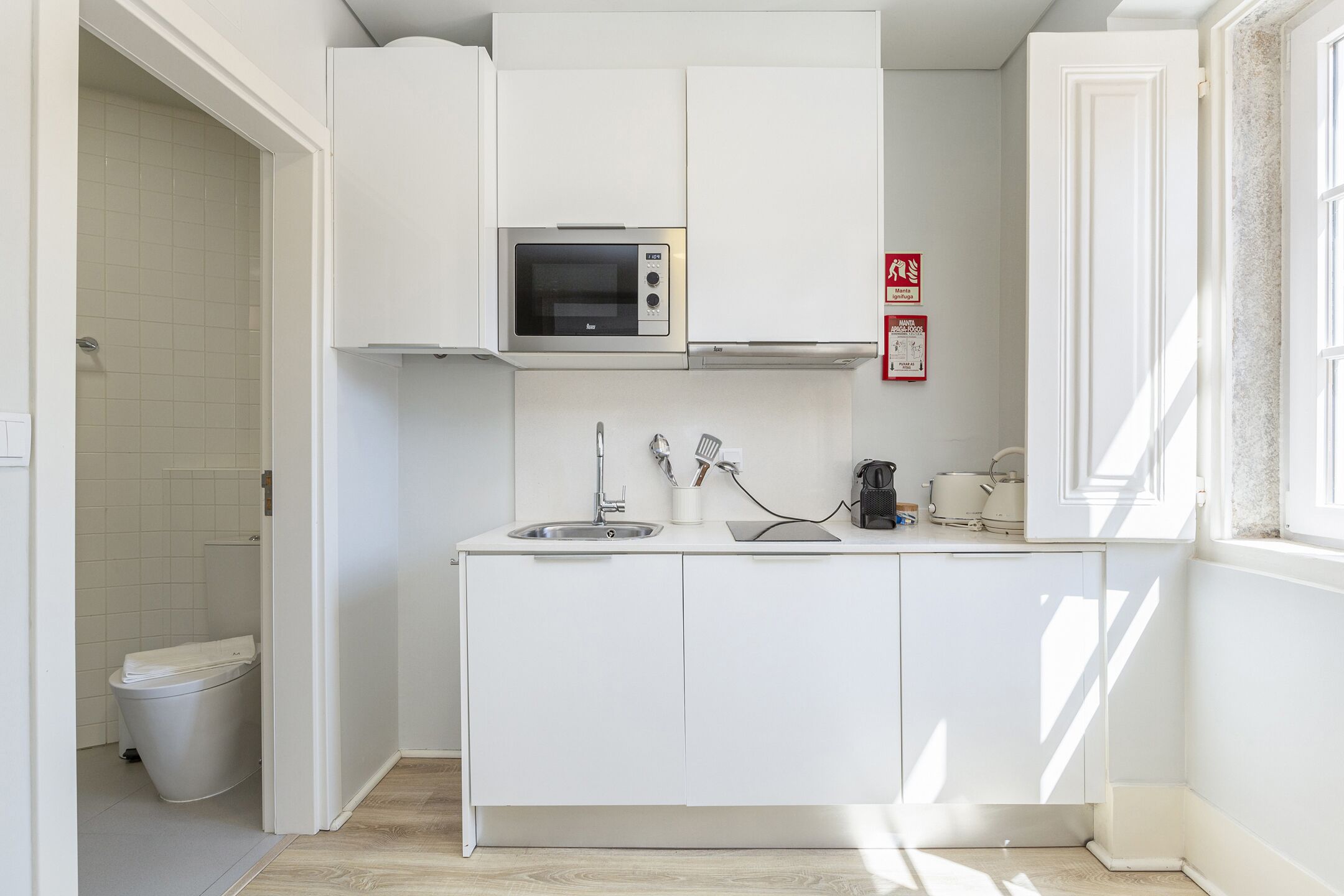 A compact kitchen with white cabinets, a microwave, a sink, and a coffee maker.