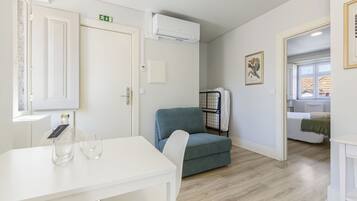 Ein Zimmer mit einem weißen Tisch, einem blauen Stuhl, einem weißen Sofa und einem Bett mit grüner Decke.