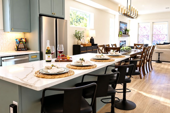 A modern kitchen with a central island, dining chairs, and a long table set for a meal. - Your 5‑Bedroom, 4‑Bath Retreat, Comfort, Style & Fun for Groups (Indianapolis)