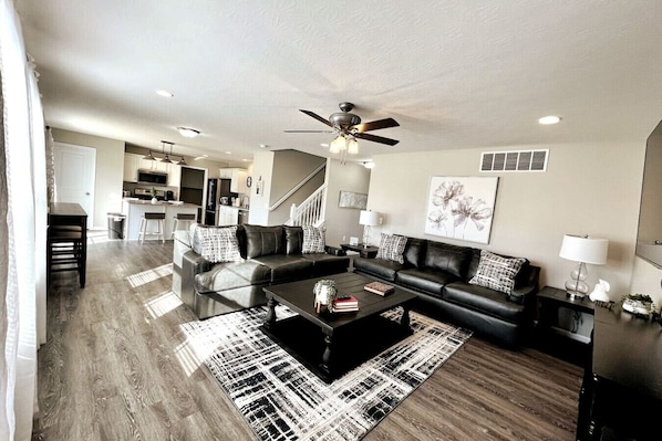 A modern living room with a sectional sofa, a coffee table, and a dining area in the background.