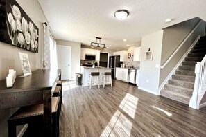 A modern kitchen with white cabinets, a central island, and a staircase leading to another level. - NEW Exec Home in Germantown, OH (Germantown)