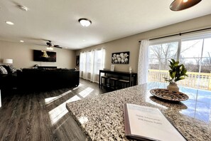 A modern living room with a dark sofa, a flat-screen TV, and a dining area with a table and chairs.