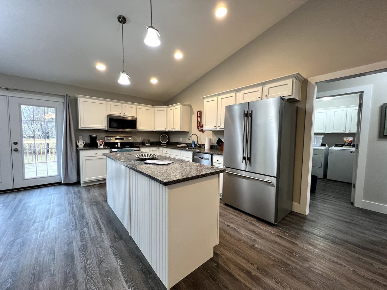 A modern kitchen with a central island, stainless steel appliances, and a view to the backyard.