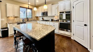 A kitchen with white cabinets, a granite island, stainless steel appliances, and pendant lighting.