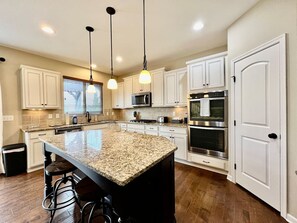 A kitchen with white cabinets, a granite island, stainless steel appliances, and pendant lighting. - Large Executive Home In Lebanon Golf Community (Lebanon)