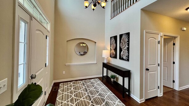 A spacious foyer with a chandelier, a console table with a lamp, and a large patterned rug.