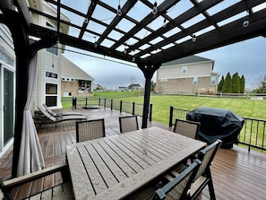 Un patio cubierto con una mesa, sillas, una parrilla y vistas a una zona residencial.