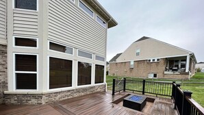A wooden deck with a fire pit, a brick house with a garage, and a second-story balcony.