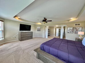 Un dormitorio con una cama grande, ventilador de techo, televisión y vestidor.