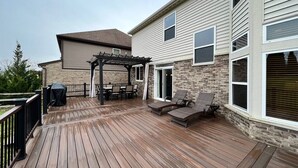 En træterrasse med udendørs møbler, en pergola og en mur af mursten.