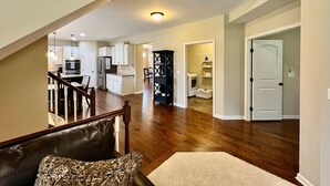 A spacious living area with a wooden staircase, a kitchen in the background, and a door leading to another room.
