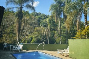 A swimming pool with lounge chairs and a water feature, surrounded by lush greenery and palm trees. - Verdadeiro Paraíso Perfeito Para Relaxar e Descansar em Meio ao Verde e Natureza (Terra Preta)