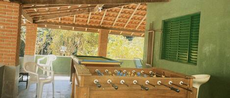 Una habitación con mesa de futbolín, mesa de billar y pared verde con contraventanas.