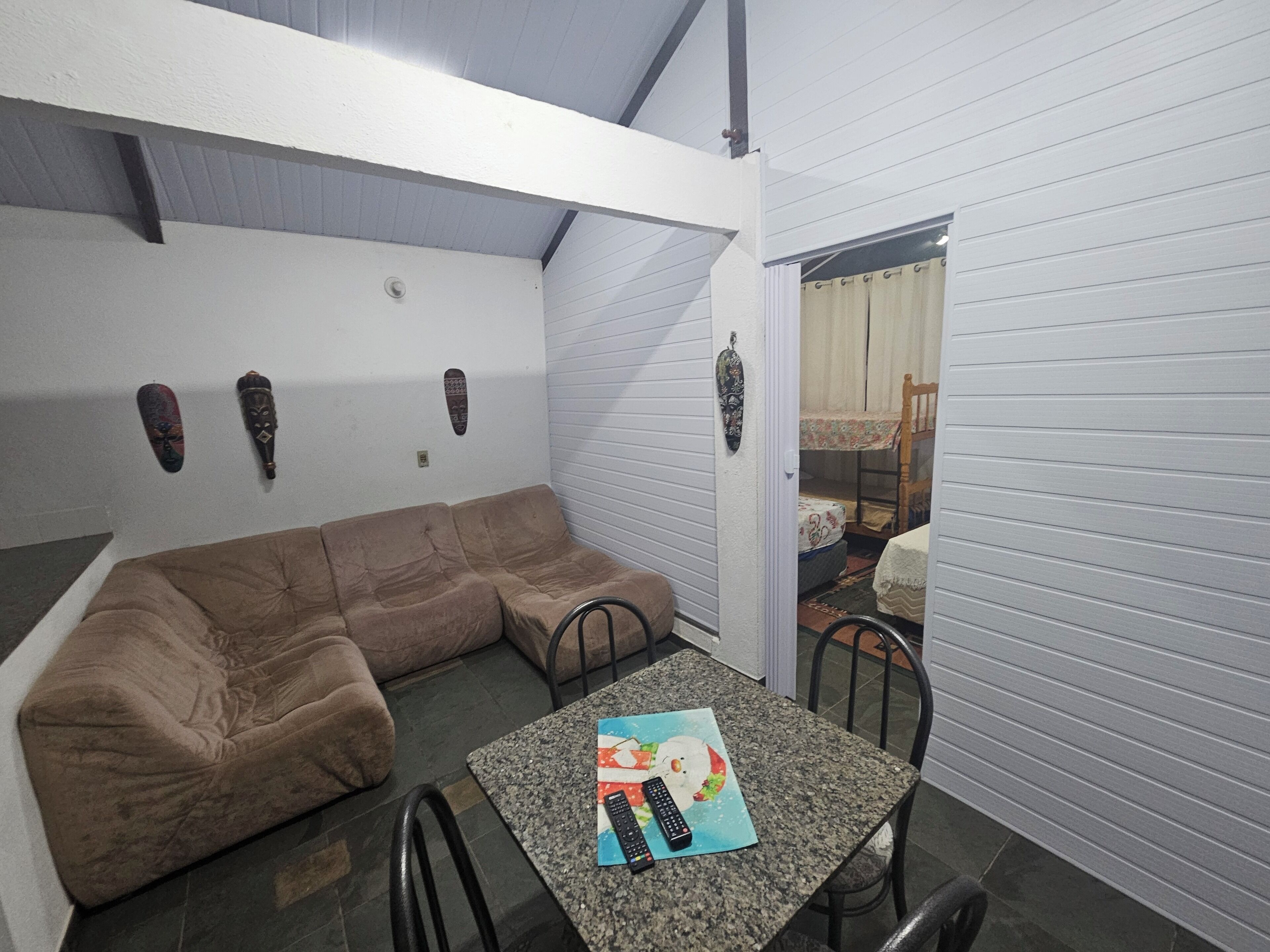 Een ruimtelijk ingerichte zithoek met een bruine modulaire bank, een klein tafeltje met een afstandsbediening, en een deur naar een andere kamer.
