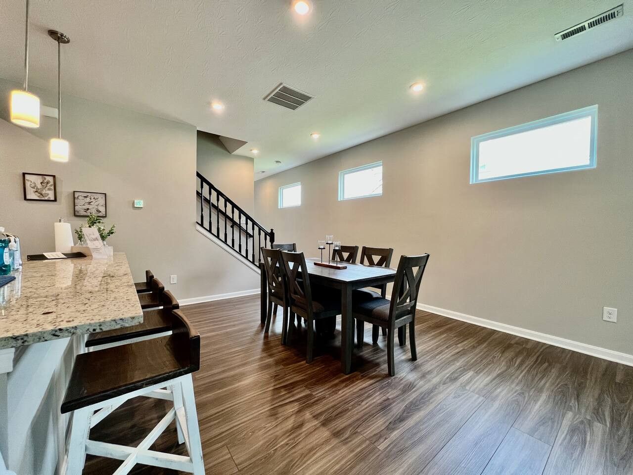 A spacious dining area with a wooden table and chairs, a kitchen counter, and a staircase leading to an upper level.