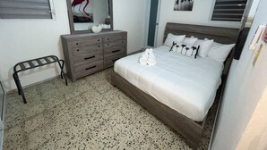 Une chambre à coucher avec un lit, une commode, un miroir et un petit tabouret.