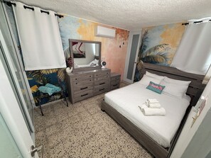 A bedroom with a bed, a dresser, a mirror, and a wall with a tropical mural. - Fajardo Family Vacation Home + Solar Backup + Game Room (Fajardo)