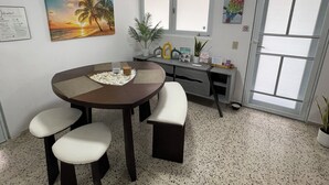 Un coin repas avec une table ronde, quatre chaises, une plante en pot et un tableau représentant un coucher de soleil.