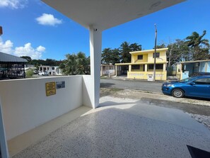 Un espace extérieur abrité, doté d’un mur blanc, d’un panneau indiquant un espace de collecte des déchets et d’une voiture bleue garée à proximité.