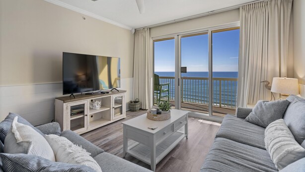 Ein Wohnzimmer mit einem großen Fernseher, einem Deckenventilator und Meerblick.