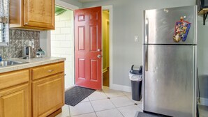 A kitchen with wooden cabinets, a stainless steel refrigerator, a red door, and a trash bin. - Savannah Home w/ Yard ~ 3 Mi to Downtown! (Savannah)
