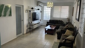 Una sala moderna con televisor de pantalla plana, un sofá de color oscuro, una mesa de centro y una lámpara de pie.