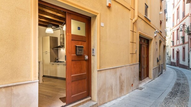 A narrow street with a building entrance featuring a wooden door and a small kitchen visible inside. - Luxury modern Studio in historic district (Cagliari)