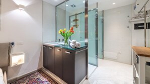 A modern bathroom with a glass shower enclosure, a sink with a glass countertop, and a vase of tulips. - Luxury modern Studio in historic district (Cagliari)