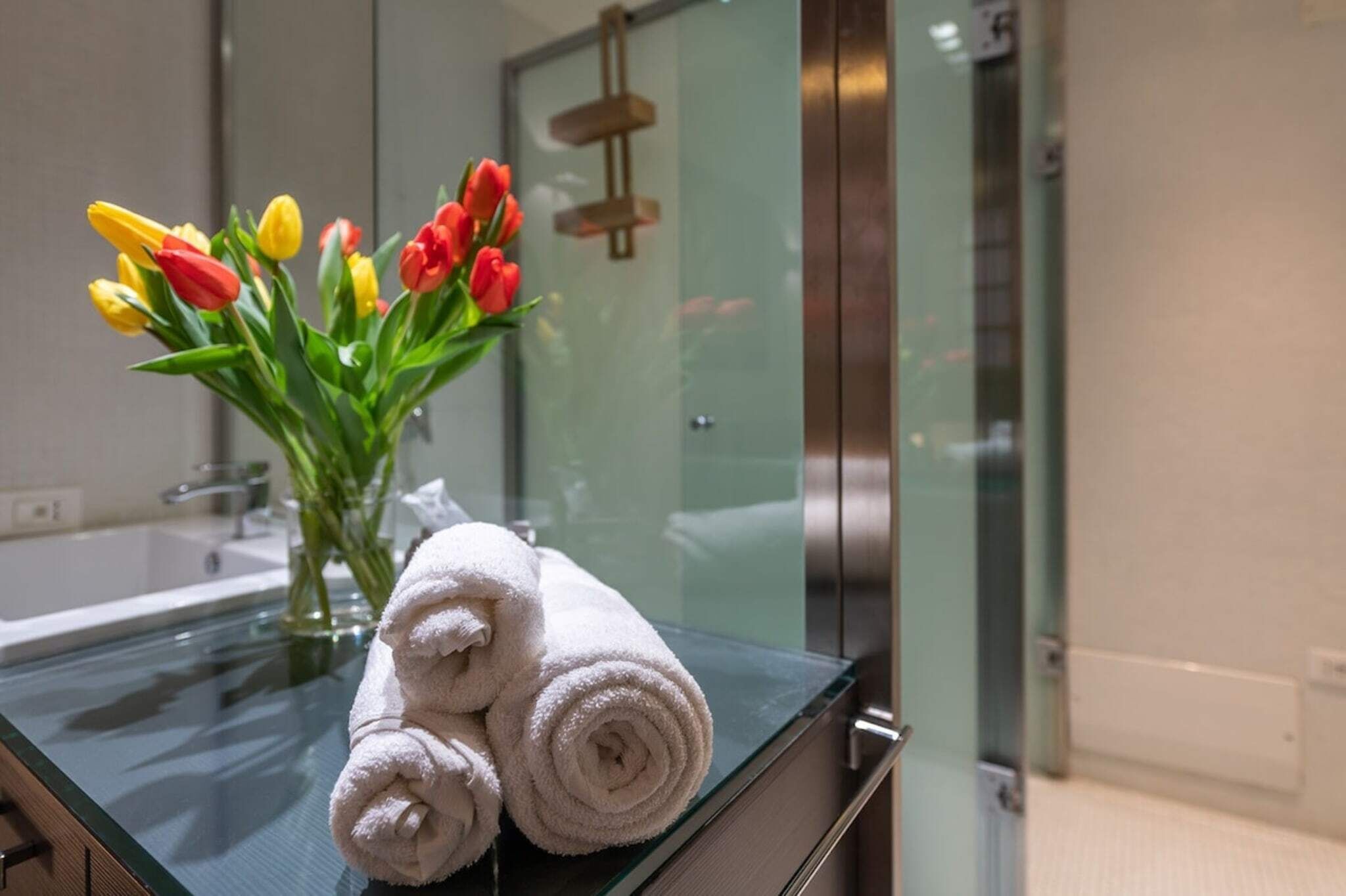 A bathroom with a glass shower enclosure, a white towel, and a vase with tulips.