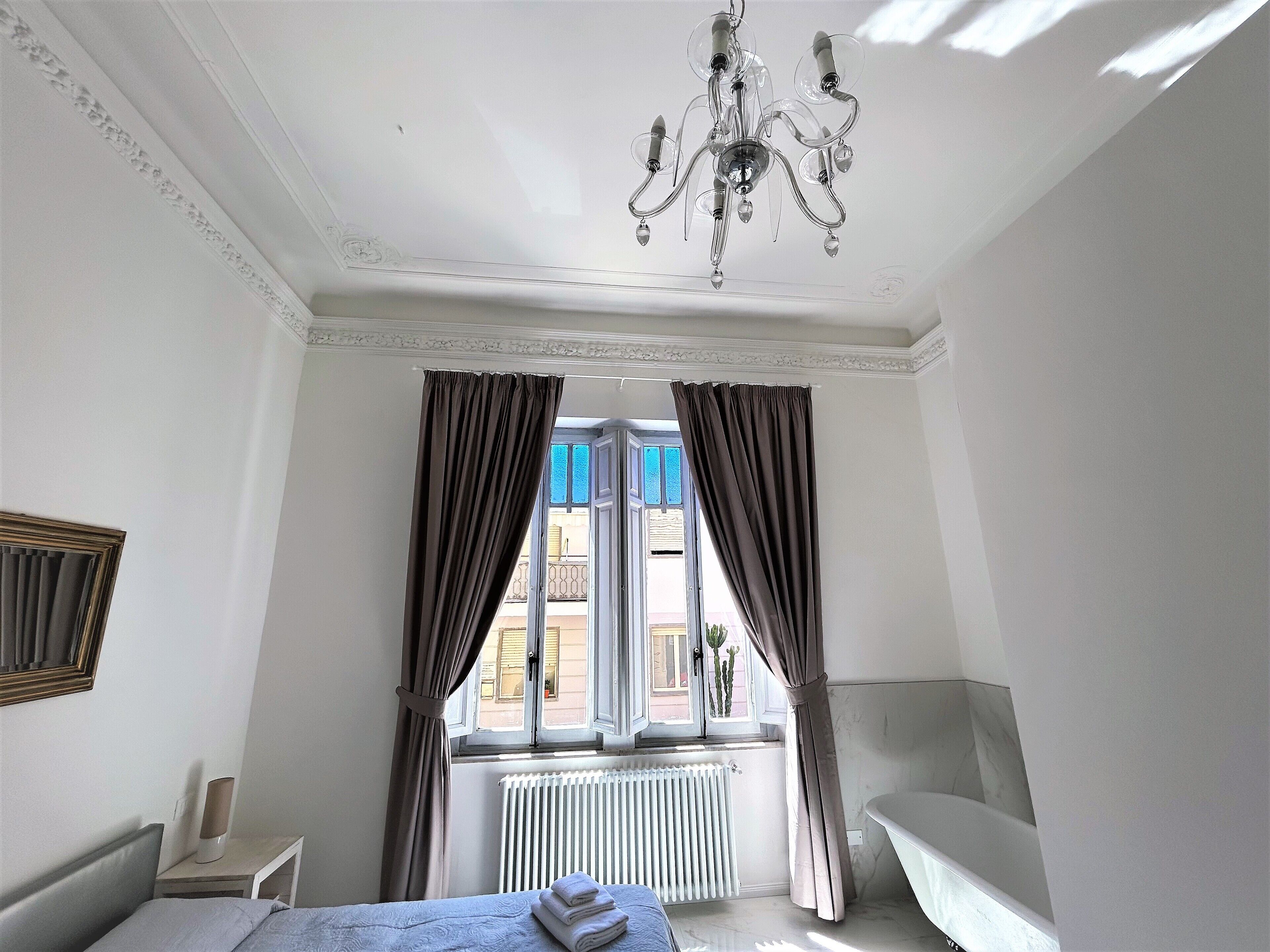 Una habitación de hotel con cama, un radiador, una ventana con cortinas y un candelabro.