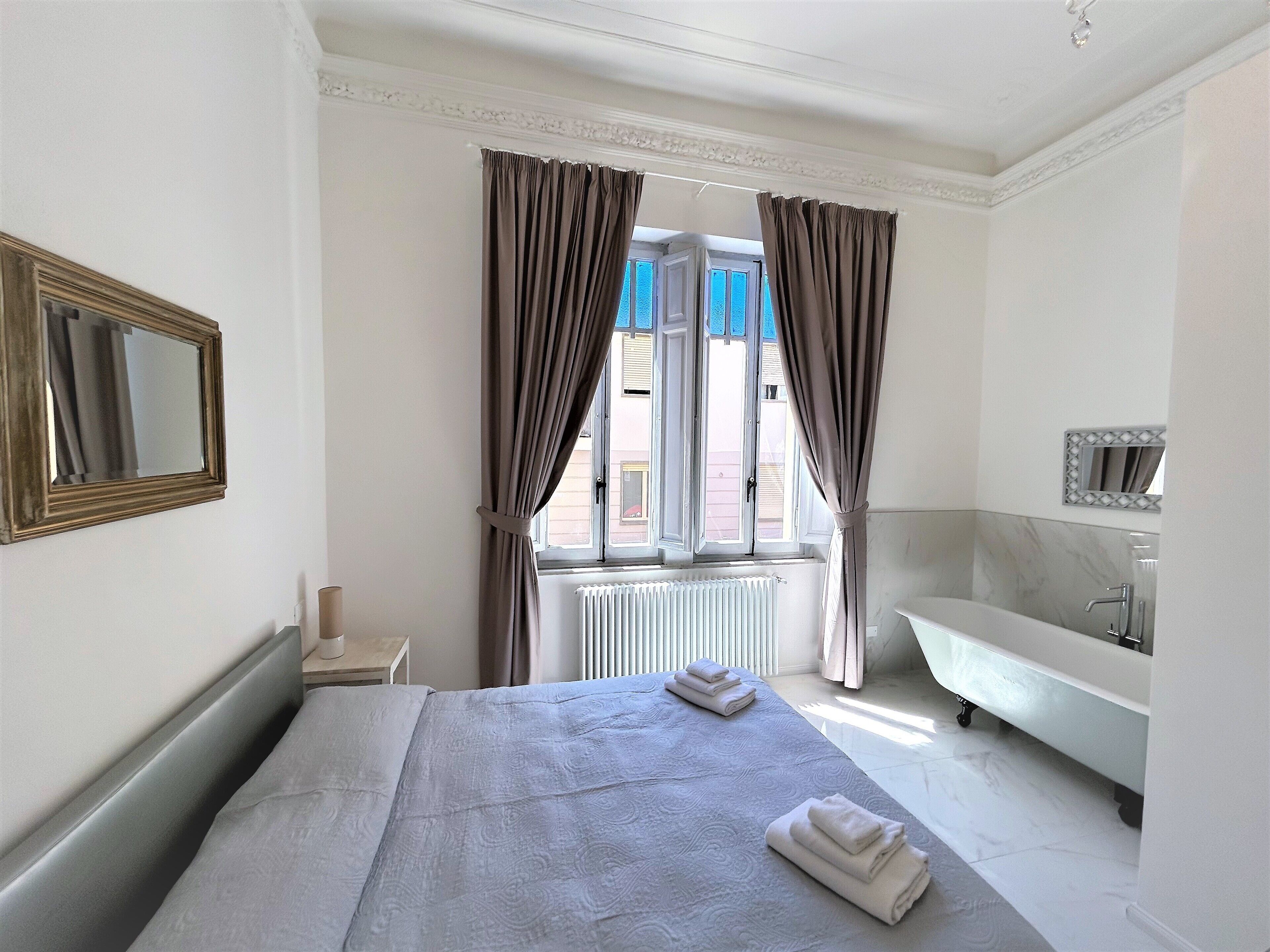 Habitación de hotel con una cama grande, un baño con bañera y una ventana con cortinas.