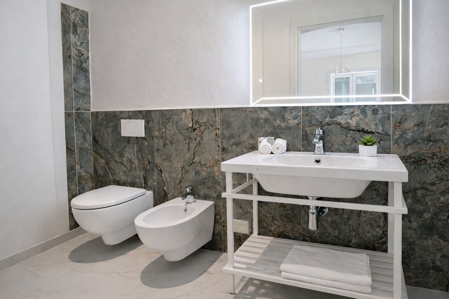 Un baño moderno con inodoro, bidé y lavamanos con resguardo de mármol.