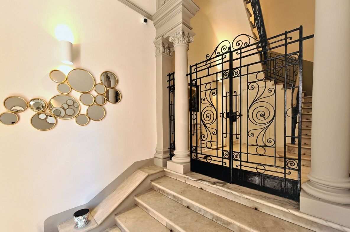 Una escalera con portón de hierro forjado, escalones de mármol y un conjunto de espejos colocados en la pared.