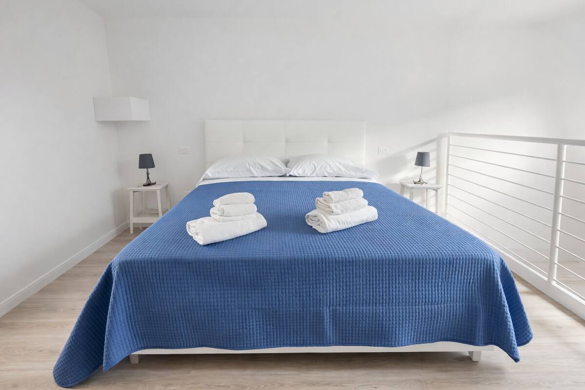 A neatly made bed with a blue bedspread, two folded white towels, and a white headboard.