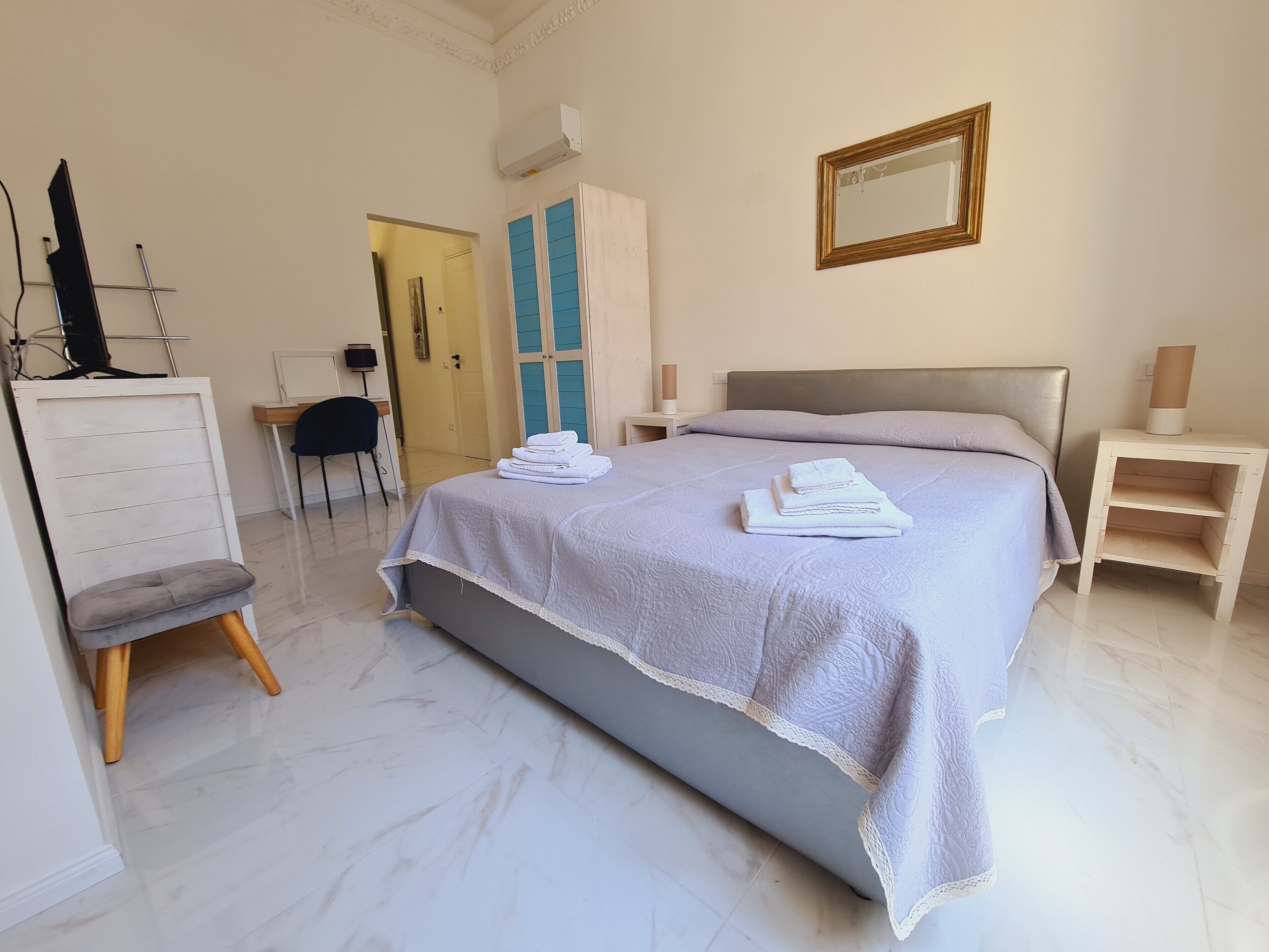 Un dormitorio ordenado con cama, mesitas de noche, una silla, un escritorio y un armario.