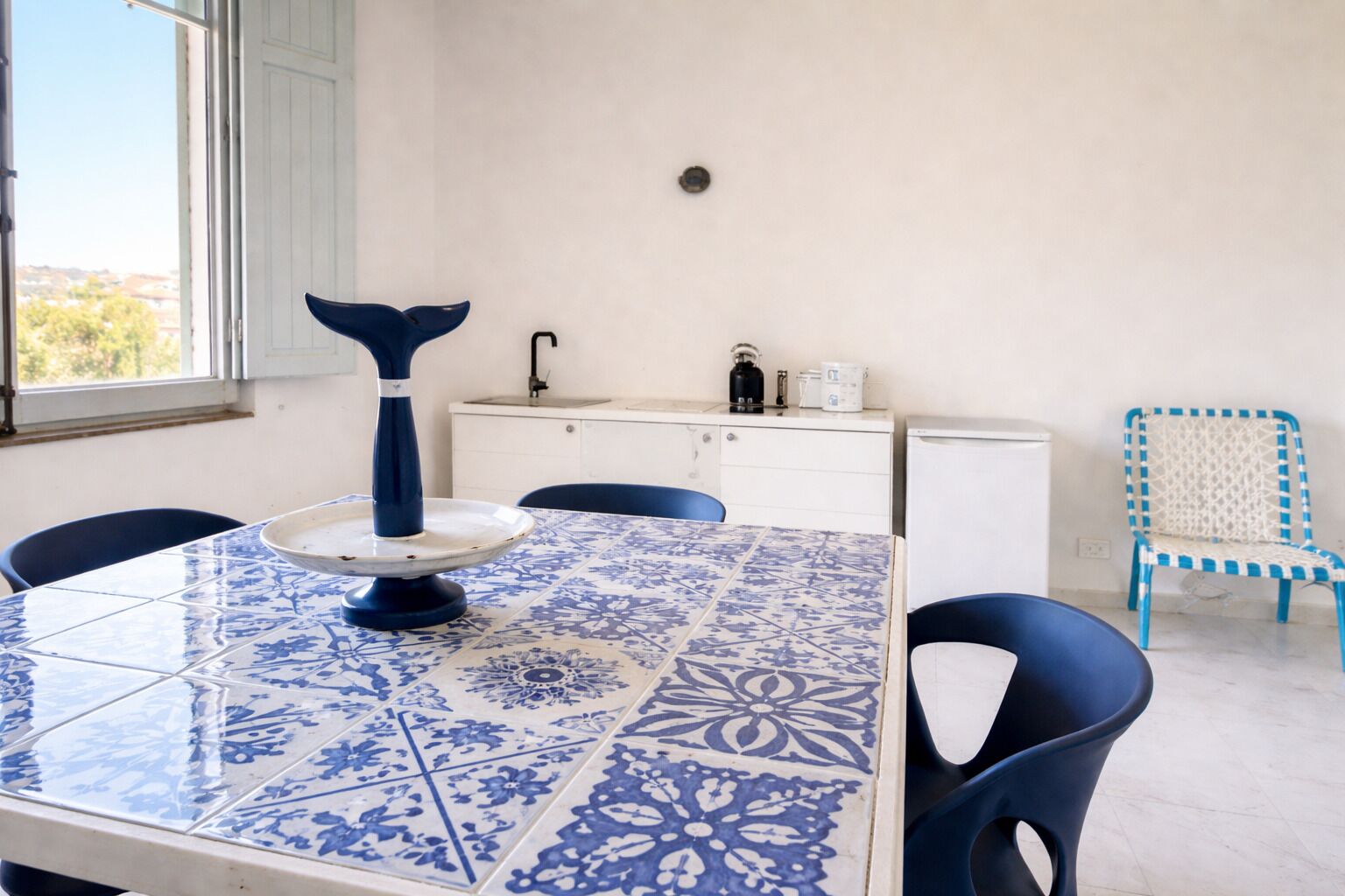 Una habitación con una mesa cubierta de azulejos, sillas, un lavabo y un refrigerador.
