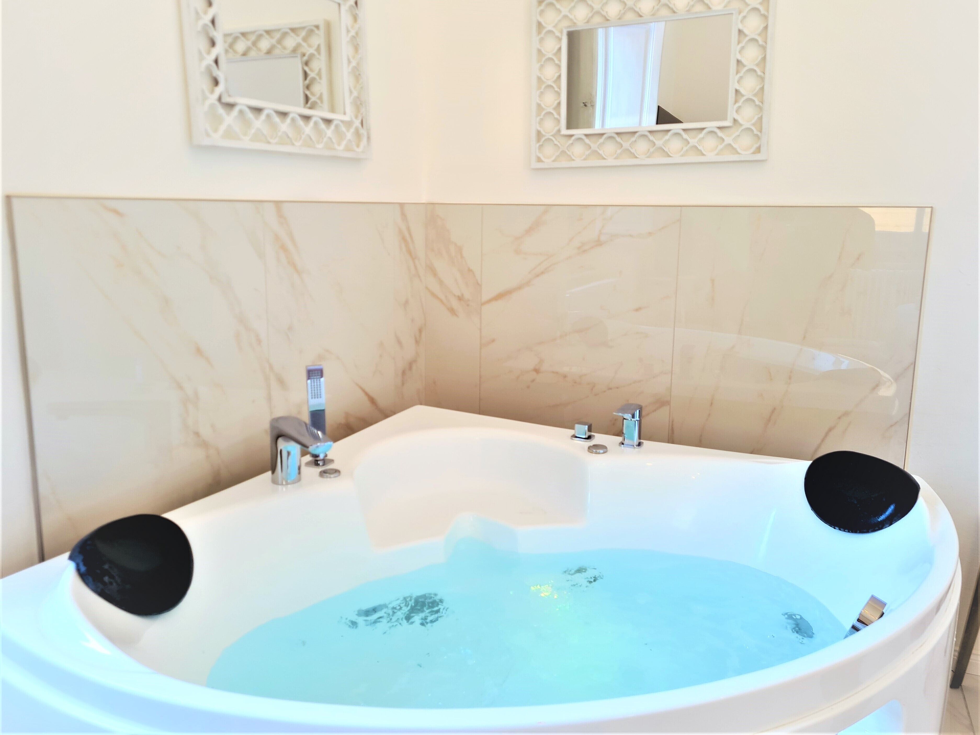 A bathroom with a marble wall, a bathtub with two black seats, and two wall-mounted mirrors.