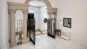 Um corredor com piso de mármore, colunas clássicas e portão de ferro forjado preto.