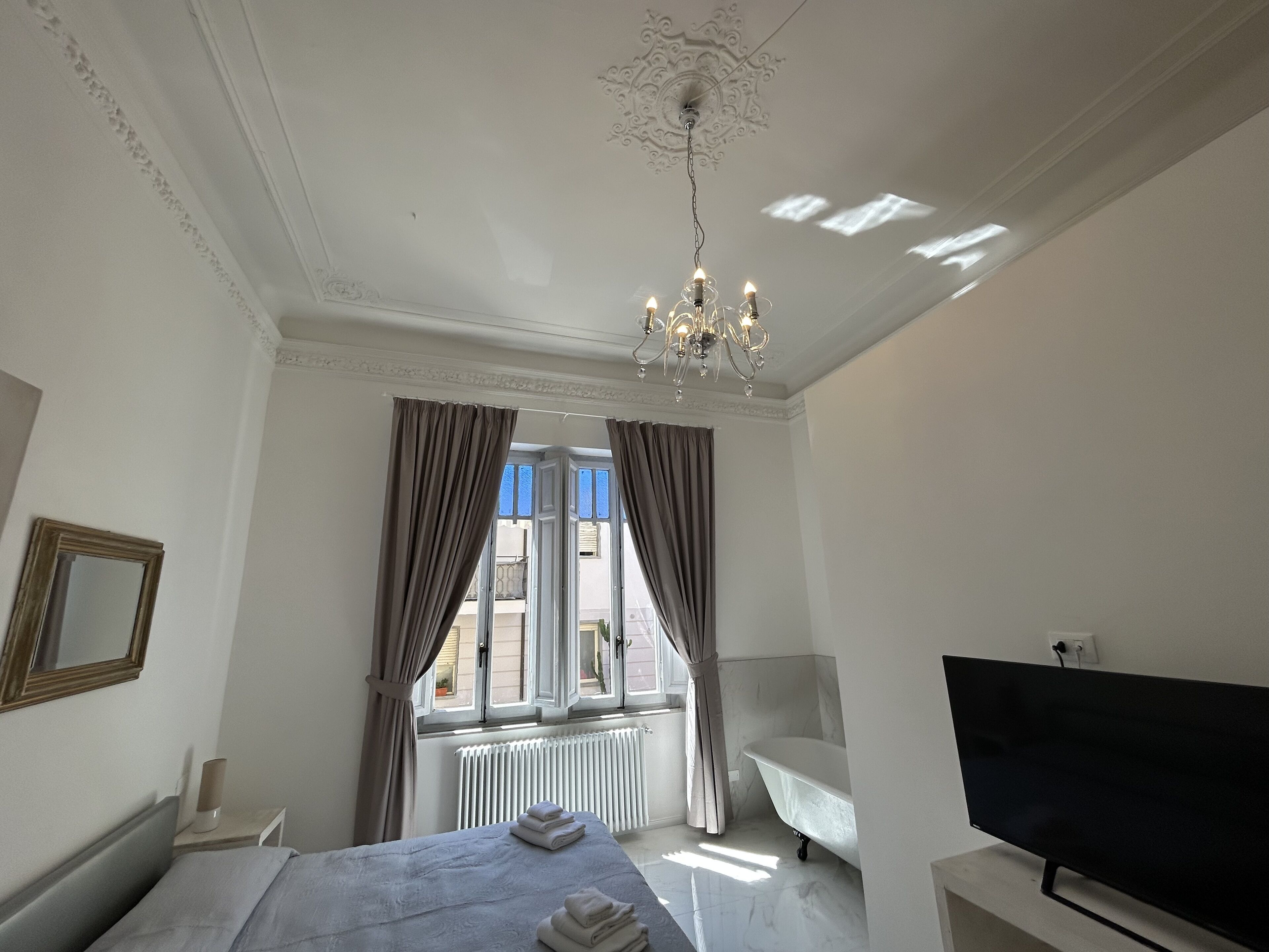 Una habitación de hotel con una cama, televisor, bañera y una ventana con cortinas.