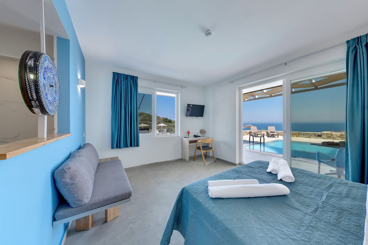 Une chambre d’hôtel avec un lit, un bureau, une chaise, une télévision et une vue sur la mer.