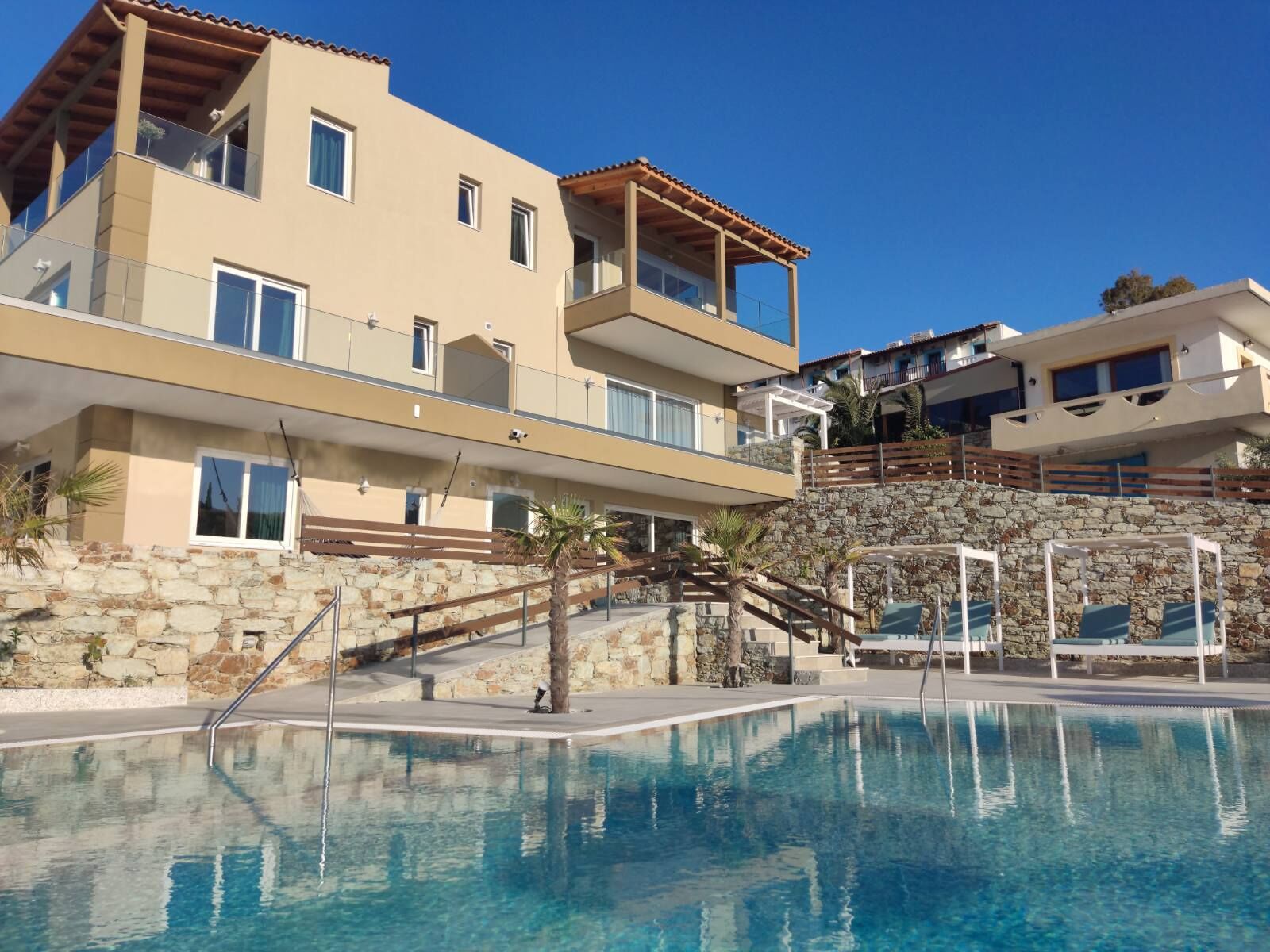 Un hotel moderno con zona de piscina, paredes de piedra y varios balcones.
