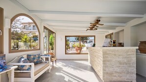 A spacious room with a large window, a stone counter, a white sofa with patterned cushions, and a ceiling fan.