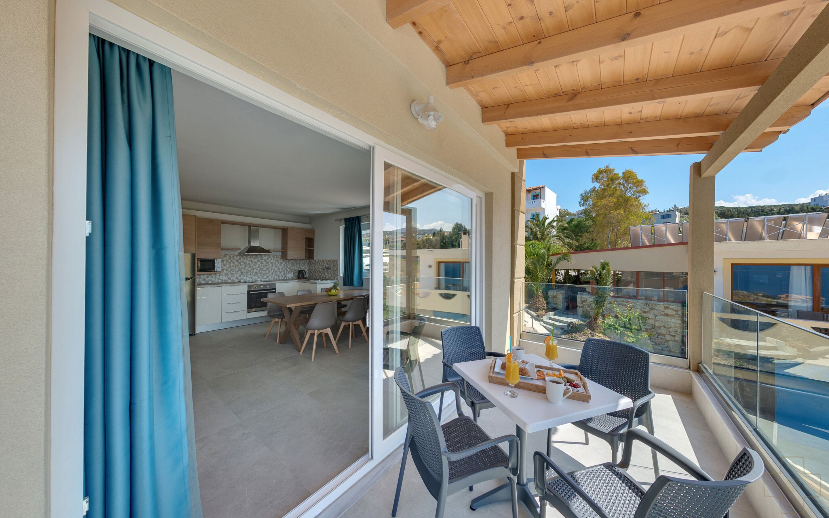 Un balcon avec une table préparée pour le petit-déjeuner, une cuisine en arrière-plan et une vue sur les environs.