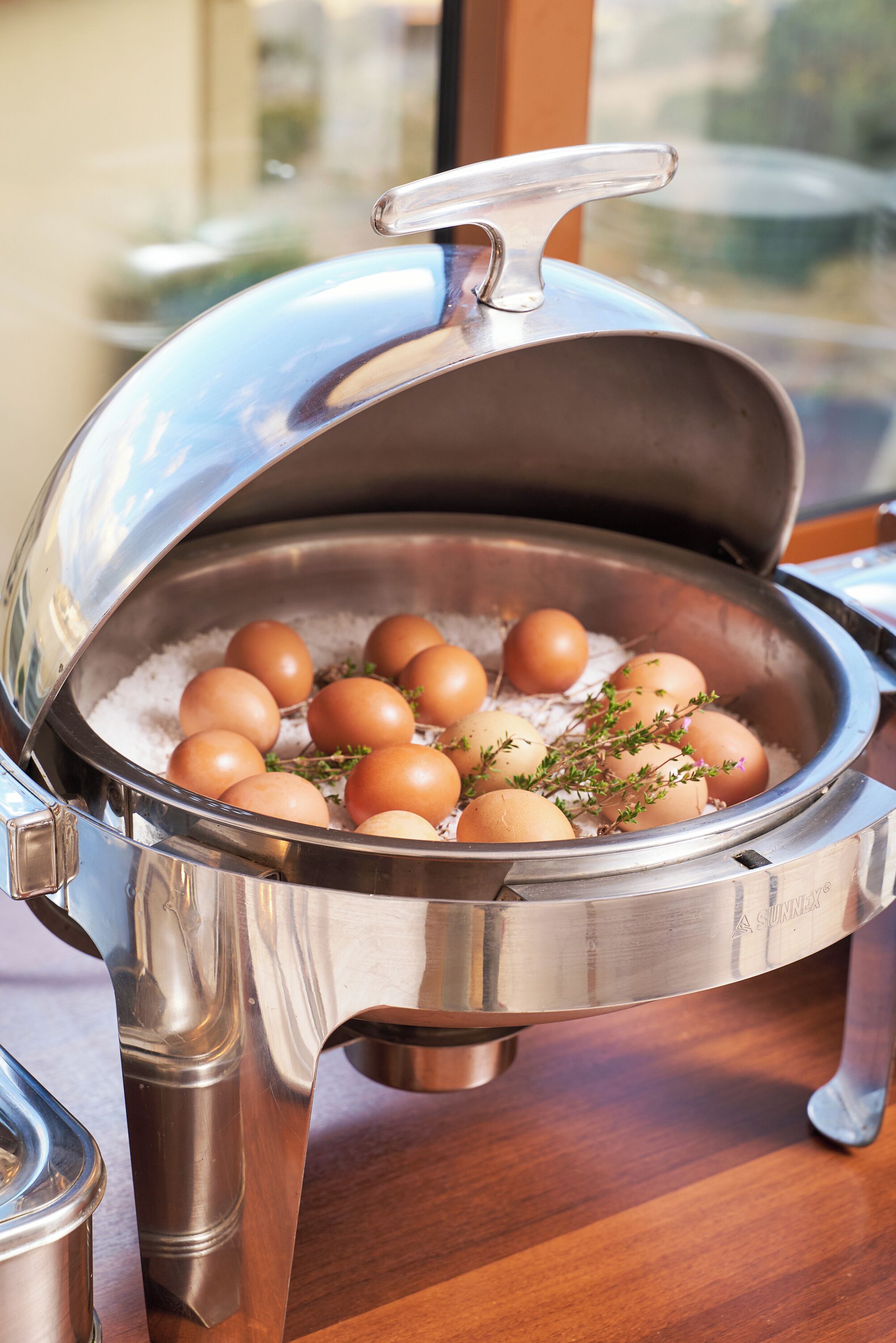 Una mesa de buffet con un recipiente metálico que contiene huevos y hierbas.