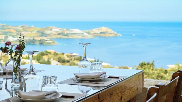 A dining table set with plates, cutlery, and glassware, overlooking a coastal landscape.