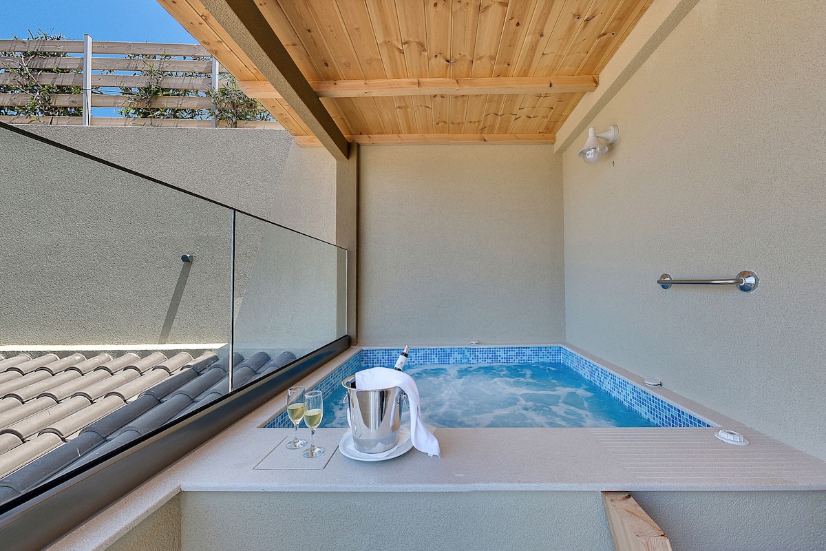 Un petit espace privé avec un jacuzzi, séparé par une paroi en verre, un seau en métal et deux verres de vin blanc.