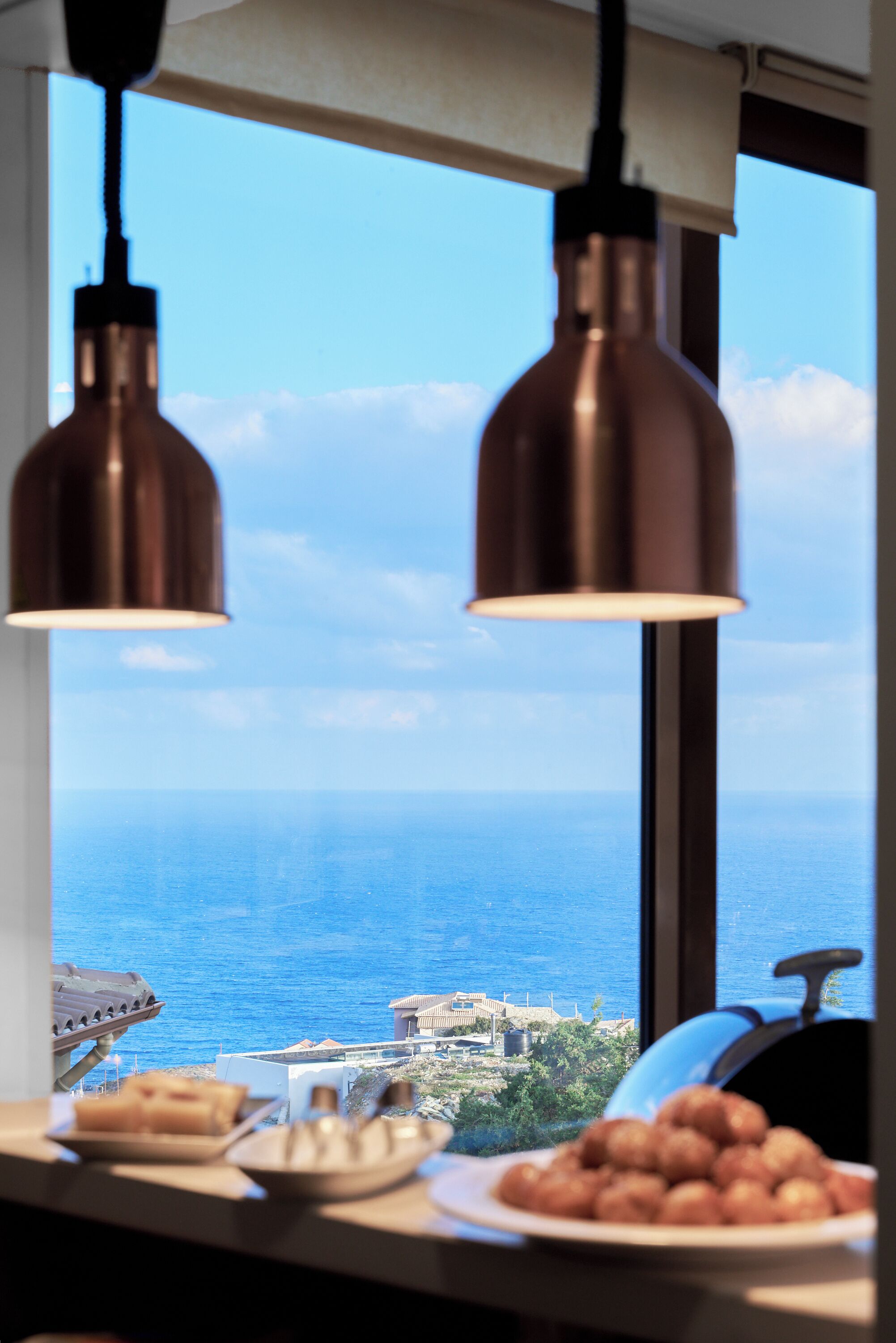 Eine Küche mit Meerblick, zwei hängende Kupfer-Pendelleuchten und ein Teller Essen auf der Arbeitsplatte.