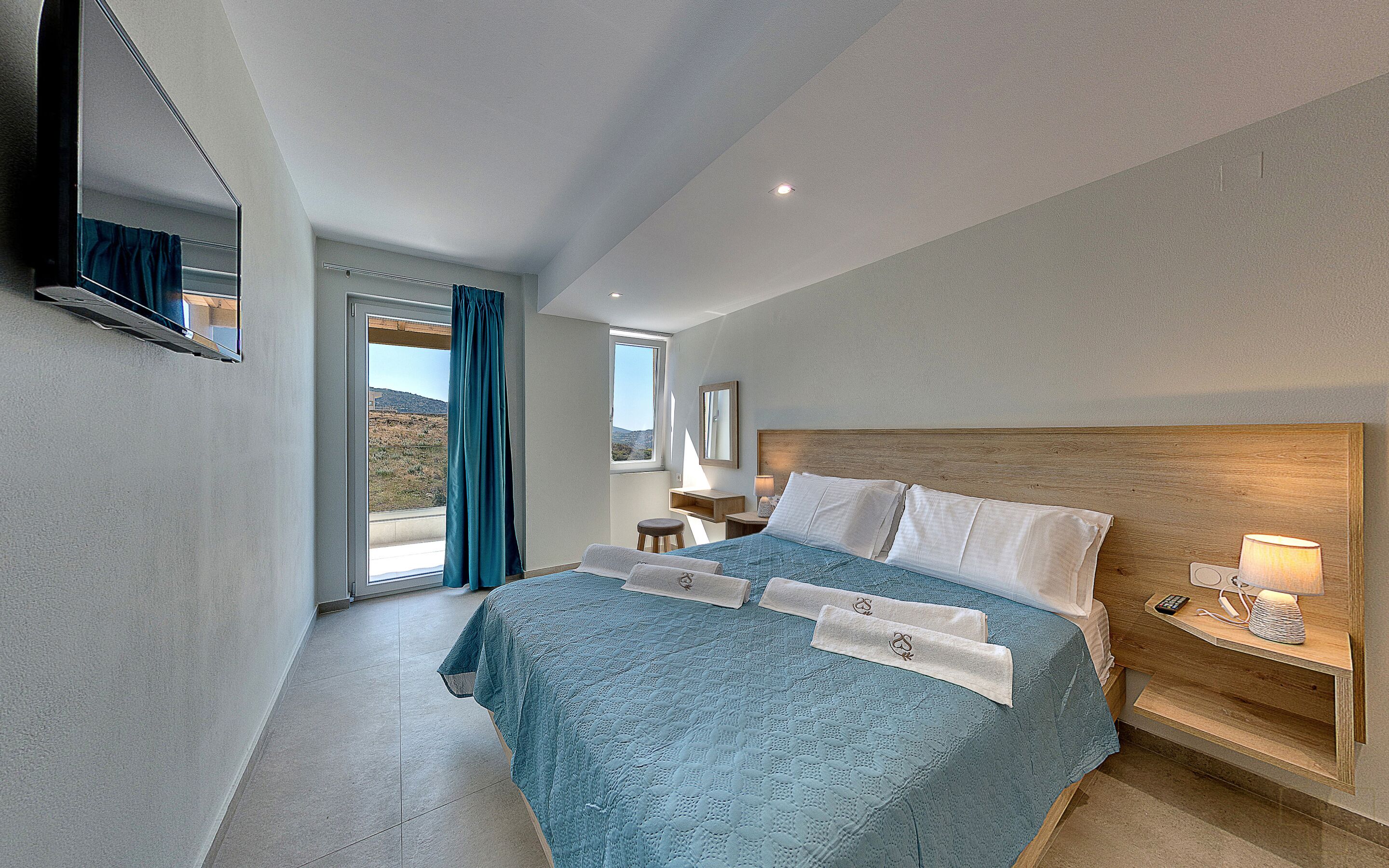 Habitación de hotel con una cama grande, una mesita de noche con lámpara, una ventana con cortinas y vistas al exterior.