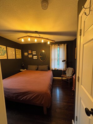 A bedroom with a large bed, a wooden chair, a mirror, and a ceiling light fixture.