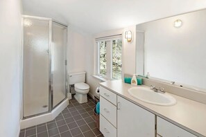 A bathroom with a shower, toilet, sink, and a window with a view of trees.